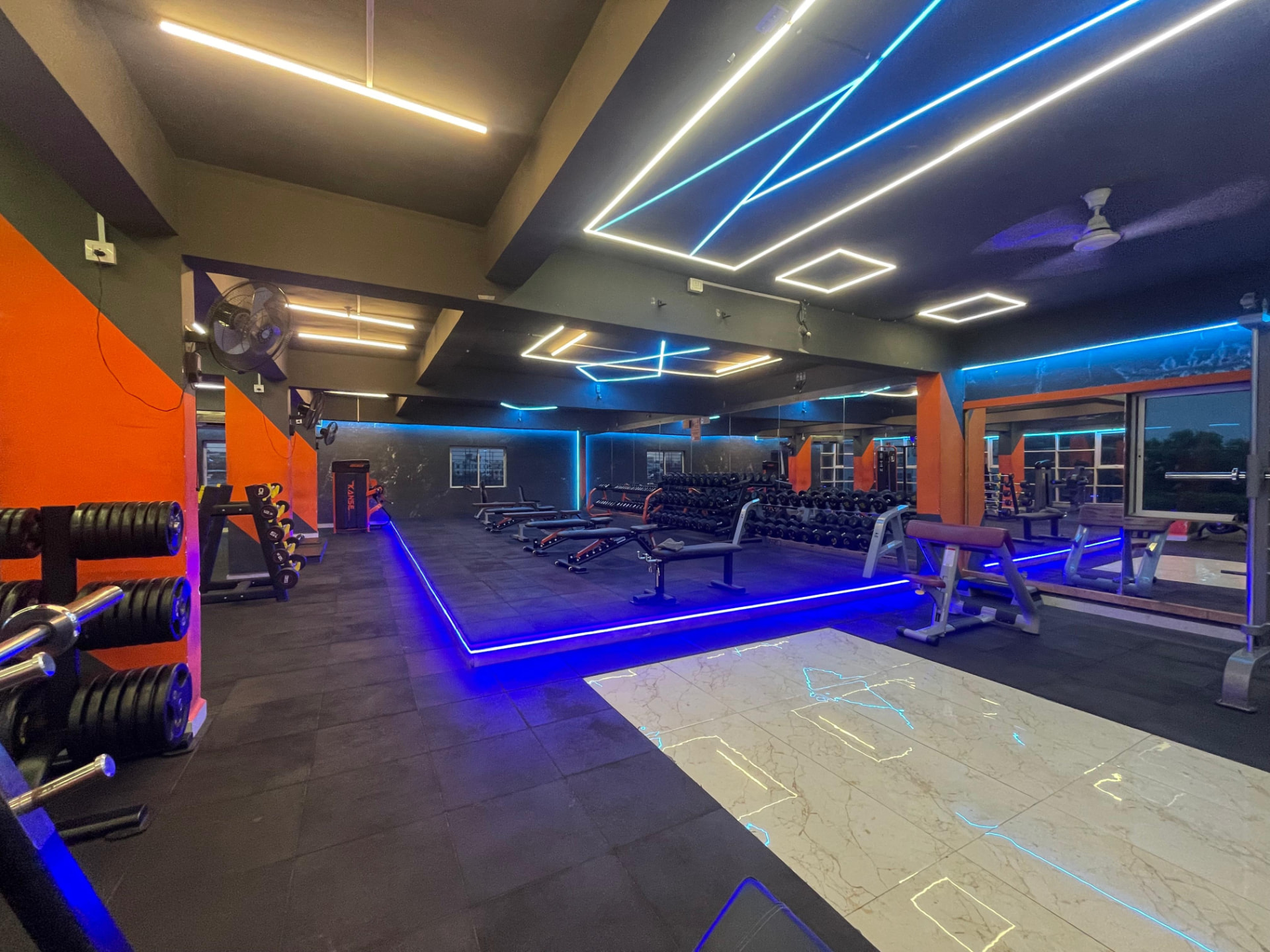 Free weights hall with adjustable benches, dumbbell racks and blue LED floor lighting at SK Fitness Gym Kharadi Free weights hall with adjustable benches, dumbbell racks and blue LED floor lighting at SK Fitness Gym Kharadi